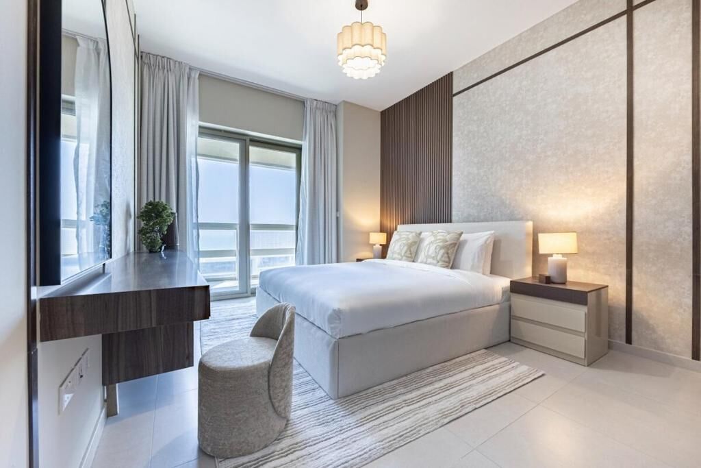 A modern hotel room with a large bed, bedside tables, a desk, and a view of the outdoors.