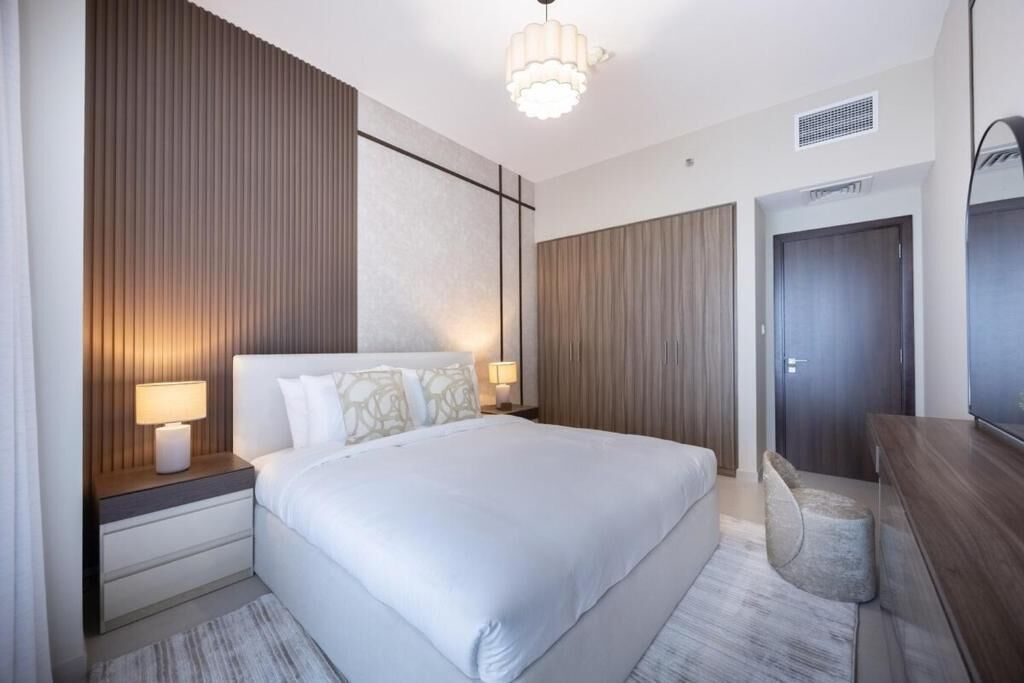 A modern hotel room with a large bed, bedside lamps, a wooden accent wall, a desk with a chair, and a wardrobe.