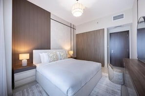 A modern hotel room with a large bed, bedside lamps, a wooden accent wall, a desk with a chair, and a wardrobe. - Bloomfields 2BR+M in Ajwan C-Saadiyat (Abu Dhabi)