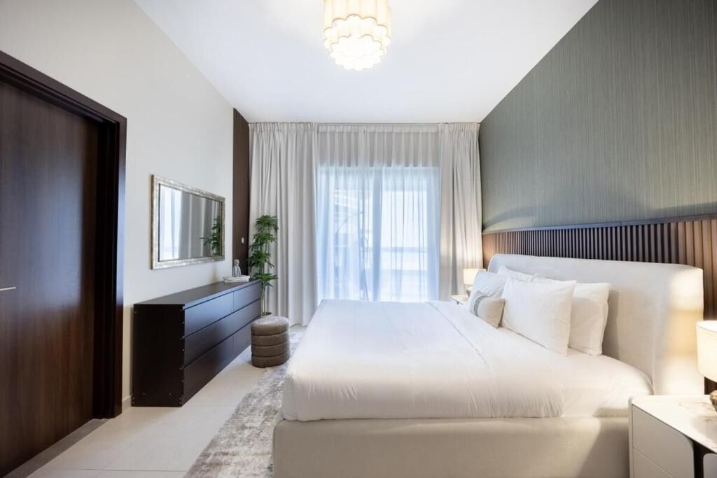 A modern bedroom with a large bed, a dresser, a mirror, and a window with curtains.