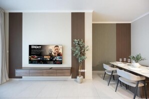 A modern living room with a flat-screen TV mounted on the wall, a dining area with a table set for four, and a potted plant. - Bloomfields 2BR+M in Ajwan C-Saadiyat (Abu Dhabi)