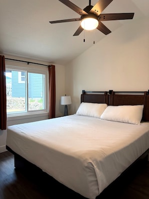 A bedroom with a bed, a ceiling fan, a window with curtains, and a lamp. - Charming Cottage 6 at Alhonna Resort (Lake Ozark)