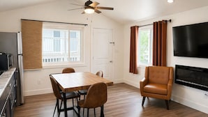 Un salon moderne avec une table à manger en bois, des fauteuils en cuir, un téléviseur à écran plat et un ventilateur de plafond.