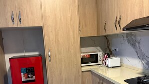 A compact kitchen with wooden cabinets, a red refrigerator, a microwave, and a gas stove. - Cozy 2-bedroom apartment located just 5 minutes from Nadi International Airport. (Martinar)
