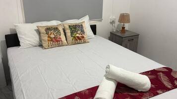 Een netjes opgemaakt bed met witte lakens, twee decoratieve kussens, een rode verenplaag en een opgerolde handdoek.