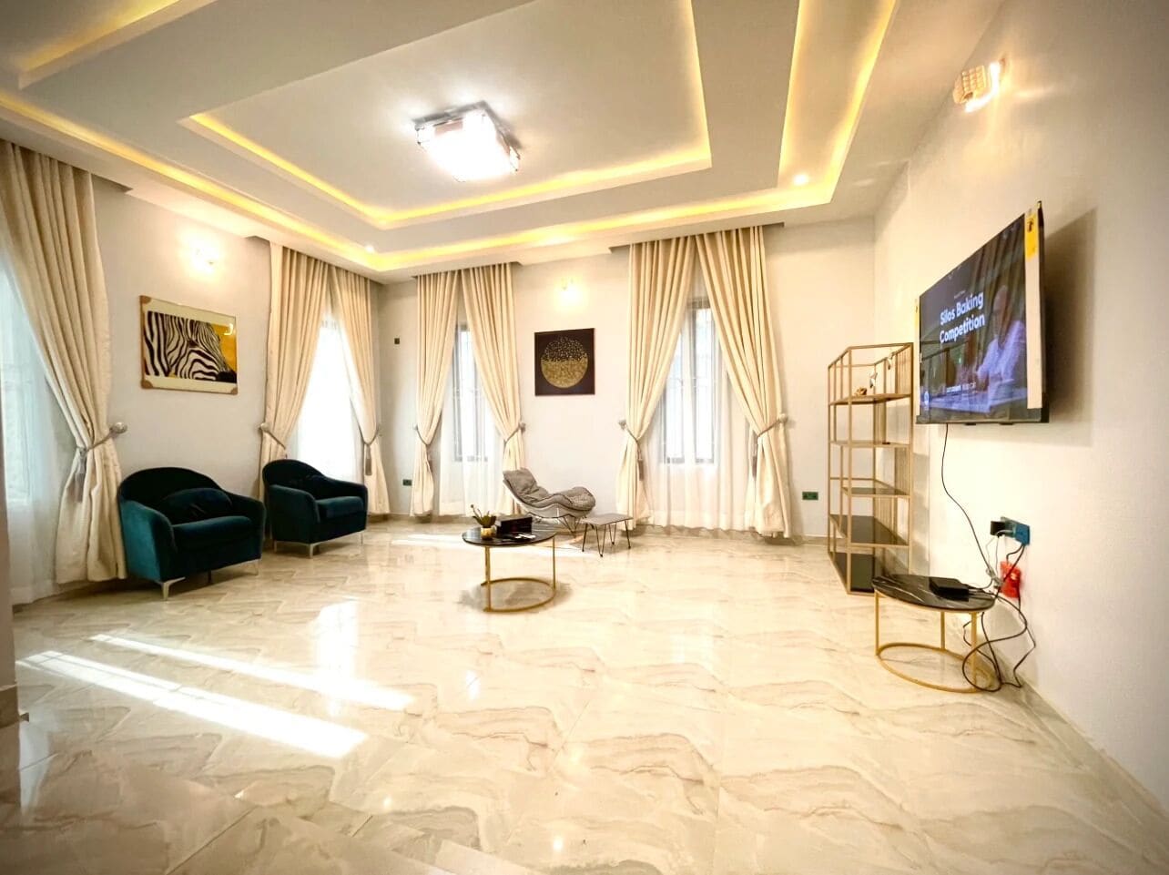 A spacious living room with a marble floor, a television mounted on the wall, and a seating area with two sofas and a coffee table.