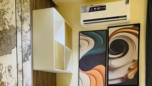 Una habitación de hotel moderna con un escritorio blanco, una silla, una cama y dos cuadros abstractos en la pared.