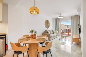A modern living room with a round wooden dining table, two sofas, and a large window with curtains. - SPECTACULAR FLAT WITH VIEWS OF THE SEA AND THE GOLF COURSE AT ISLAND DE RIVIERA (Riviera del Sol - Mijas Costa)