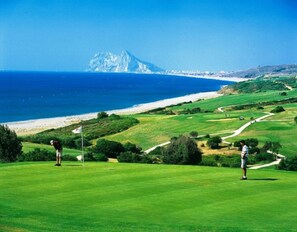 Ein Golfplatz mit Blick auf das Meer und ein Berg in der Ferne.
