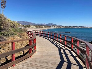 A wooden boardwalk with red railings leading to a beach. - SPECTACULAR FLAT WITH VIEWS OF THE SEA AND THE GOLF COURSE AT ISLAND DE RIVIERA (Riviera del Sol - Mijas Costa)