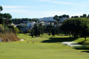 A golf course with a water fountain, trees, and buildings in the background. - SPECTACULAR FLAT WITH VIEWS OF THE SEA AND THE GOLF COURSE AT ISLAND DE RIVIERA (Riviera del Sol - Mijas Costa)