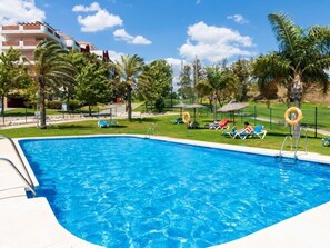 A swimming pool with a clear blue water surface, surrounded by lounge chairs and umbrellas, with palm trees and a building in the background. - SPECTACULAR FLAT WITH VIEWS OF THE SEA AND THE GOLF COURSE AT ISLAND DE RIVIERA (Riviera del Sol - Mijas Costa)