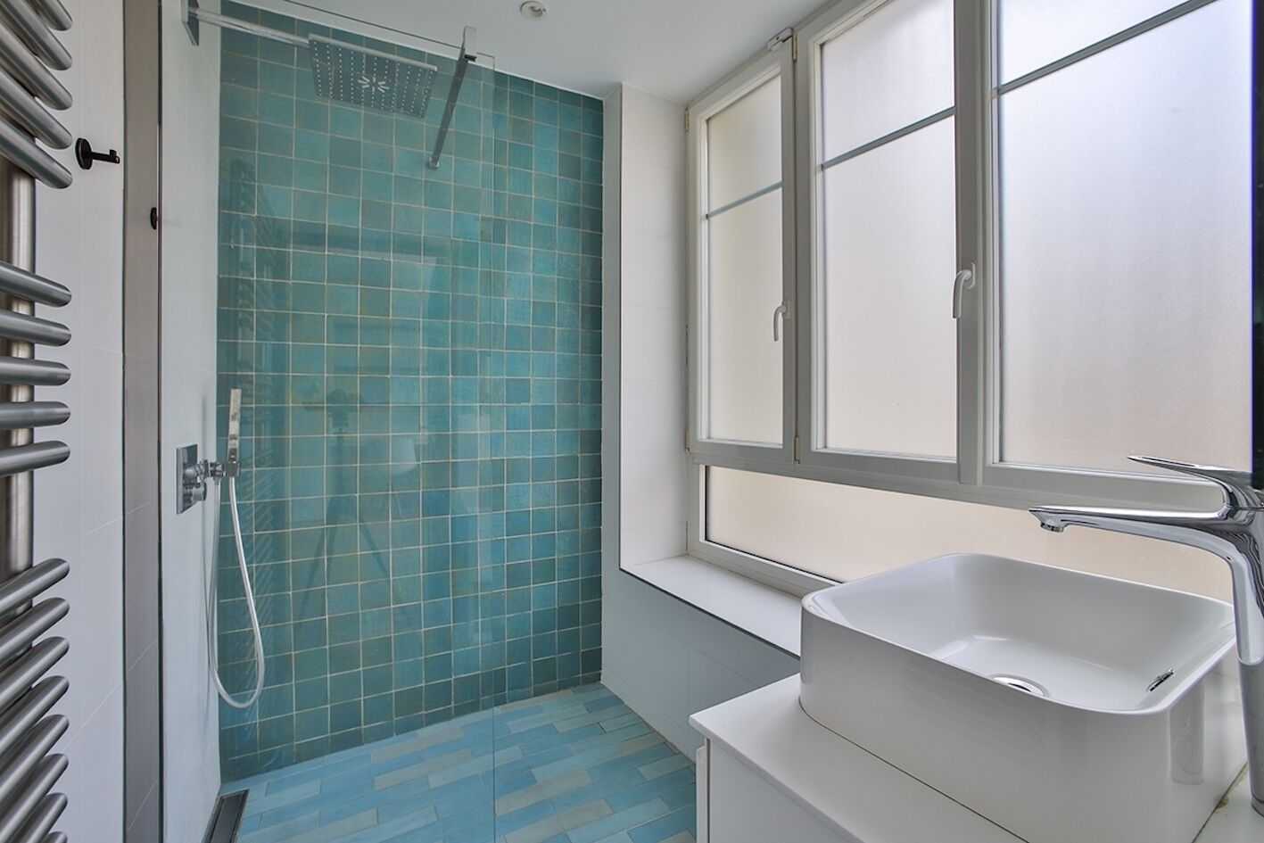 Een badkamer met een douche, een raam en een wastafel.