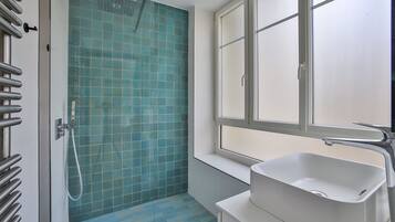 Een badkamer met een douche, een raam en een wastafel.