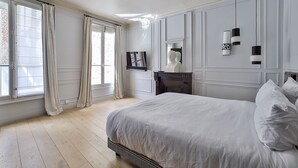 Quarto com cama grande, penteadeira, espelho e janela com cortinas.