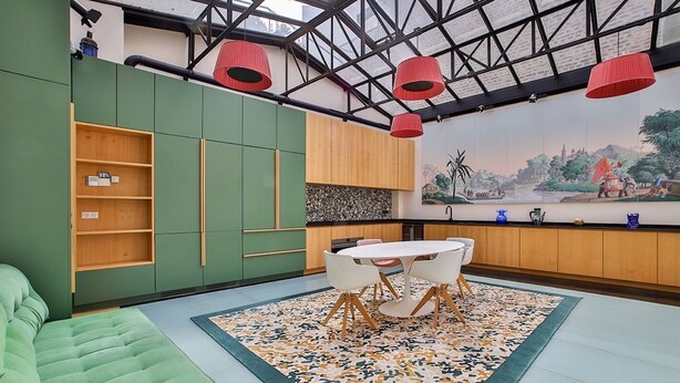 A modern kitchen with green cabinets, a dining table with chairs, and a large window with red pendant lights.
