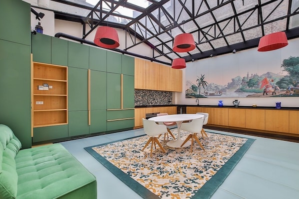 Una cocina moderna con armarios verdes, una mesa de comedor con sillas y un amplio ventanal con lámparas colgantes rojas.