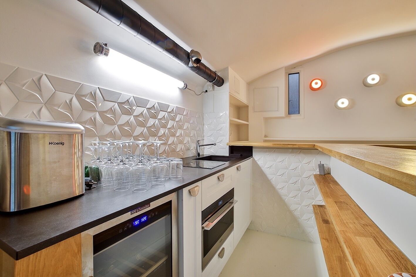 A modern kitchen with a built-in oven, a stainless steel appliance, and a countertop with glasses.