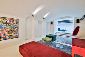 Una camera moderna con un divano rosso, un'opera d'arte colorata, un tavolo in vetro trasparente e una finestra con vista.