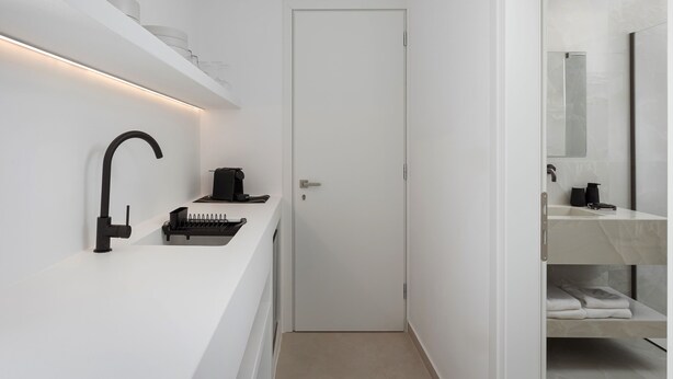 A modern bathroom with a white sink, black faucet, and a coffee machine. There is a door leading to another room. - Parolea Luxury Living Hotel (Paros)
