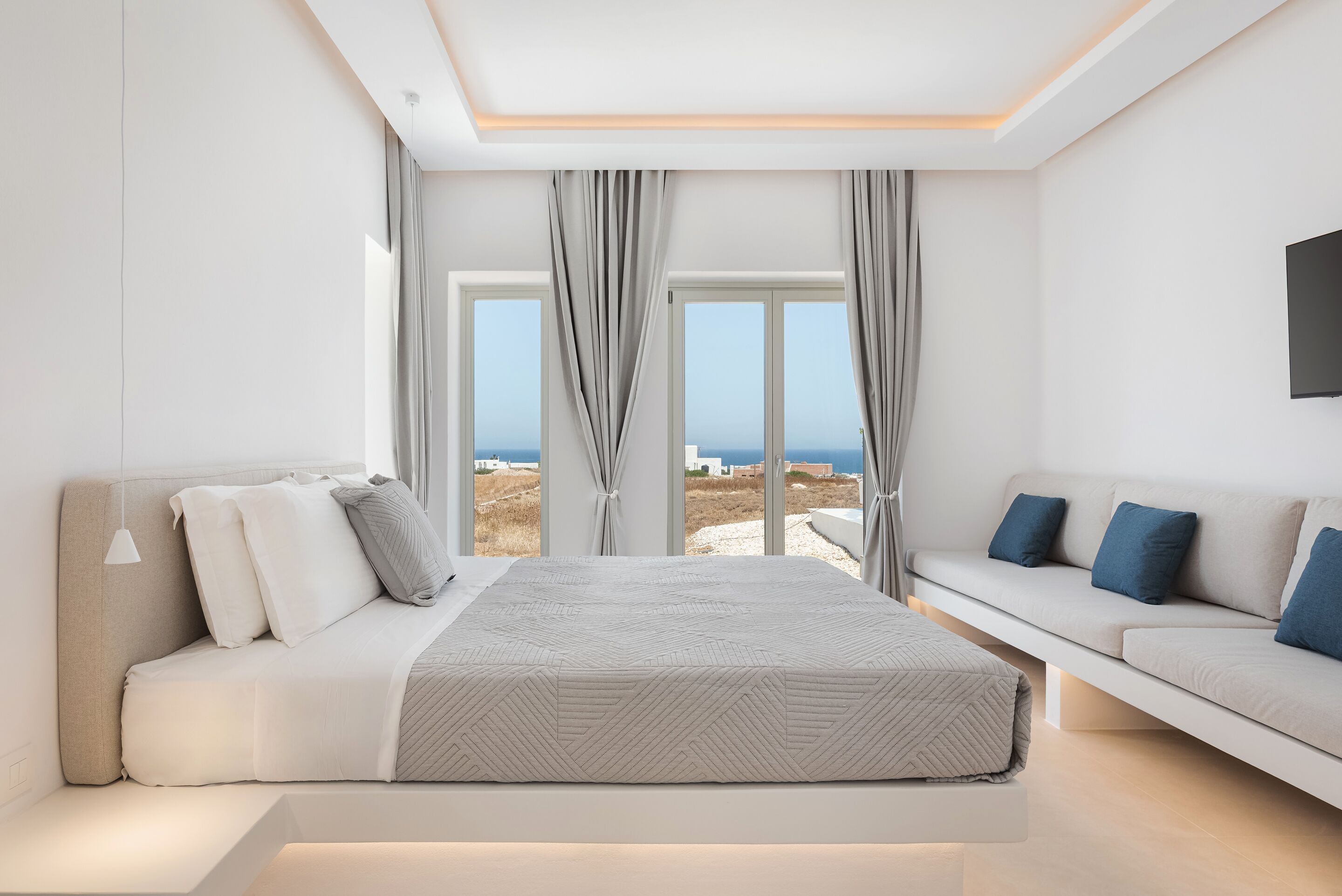 A modern bedroom with a large bed, a sofa, and a view of the sea.