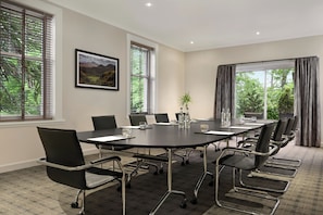 Sala de conferência com uma mesa grande, cadeiras e janelas com persianas.