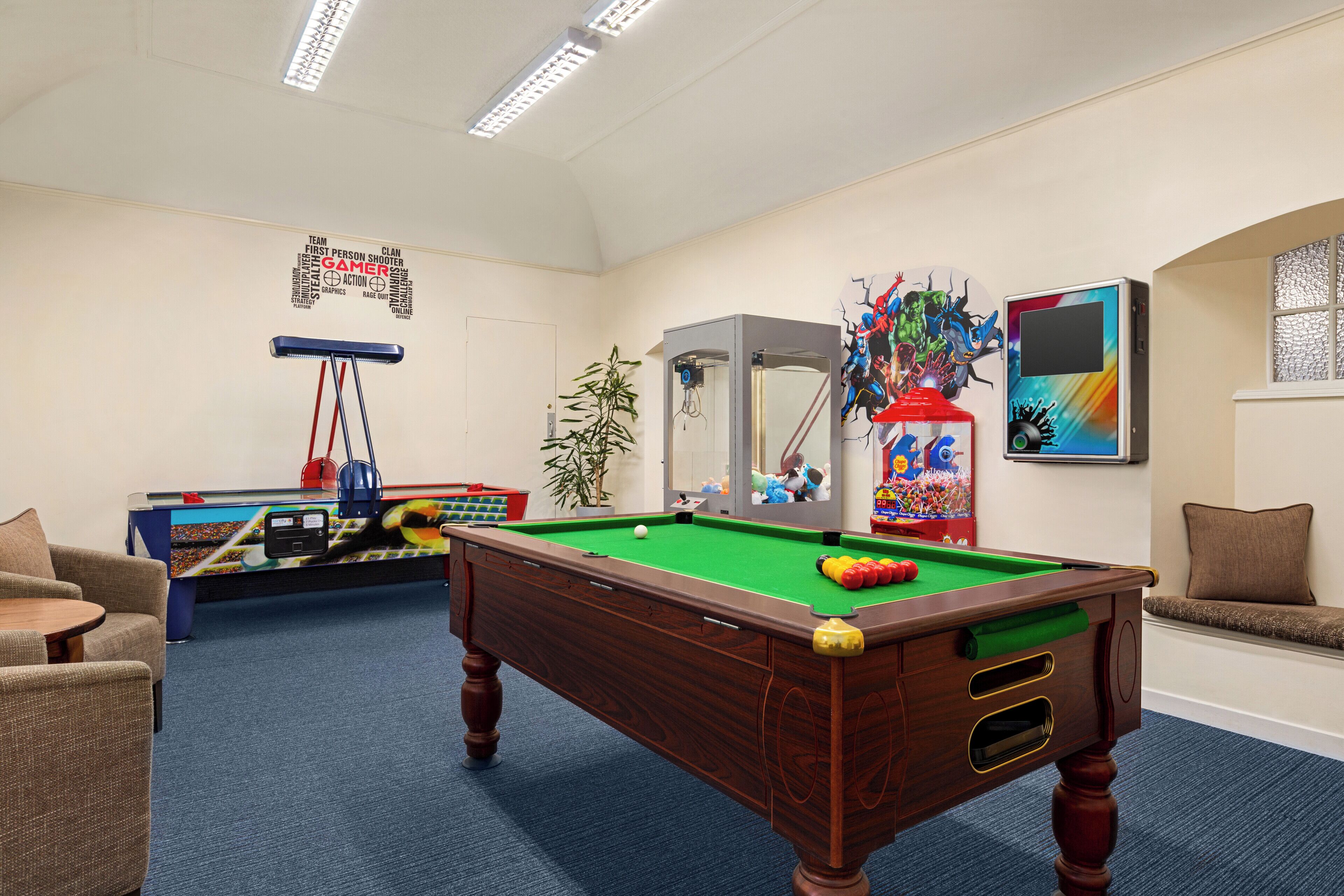 A pool table in a room with a ceiling fan, a foosball table, and a wall with a word cloud.