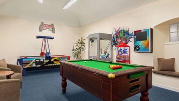 A pool table in a room with a ceiling fan, a foosball table, and a wall with a word cloud.