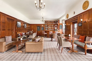 Um quarto amplo com painéis de madeira, piso xadrez, área de bar e disposições de assento, incluindo sofás e mesas.