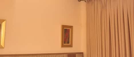 A hotel room with a bed, a headboard, a ceiling light fixture, a framed picture on the wall, and a window with curtains.