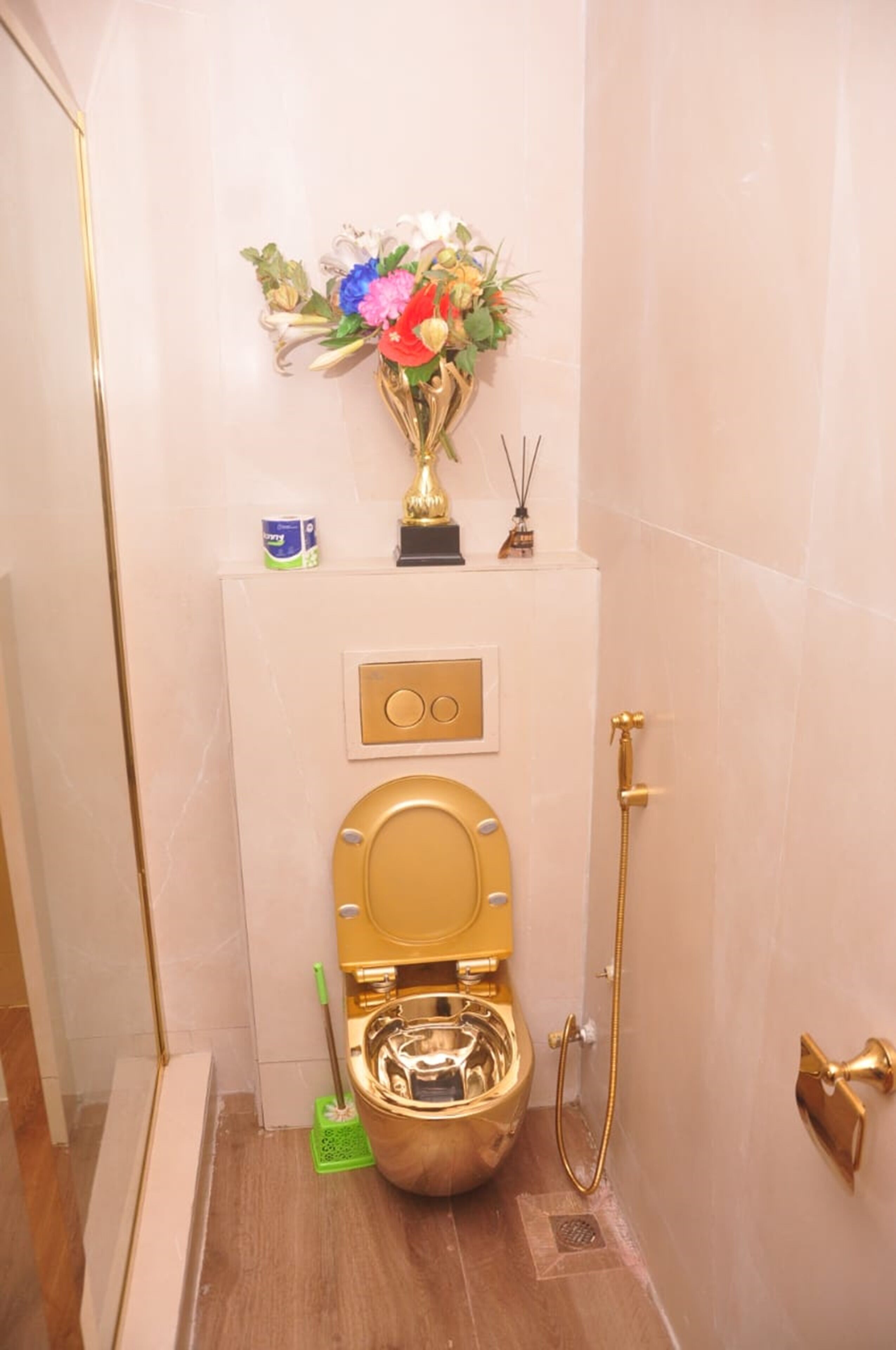 A bathroom with a gold toilet, a shower, and a decorative vase with flowers on the wall.