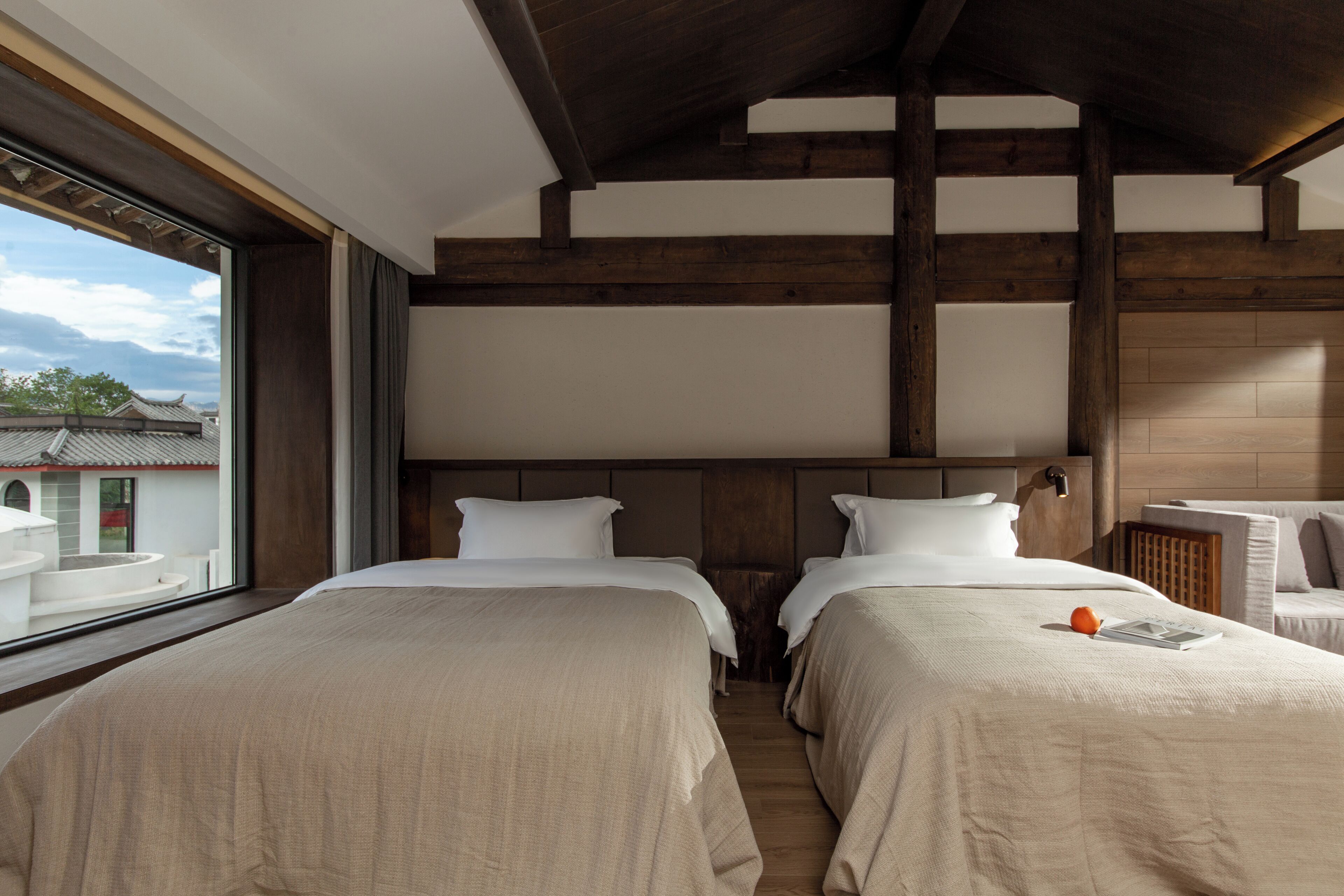 A hotel room with two beds, a large window, and a view of traditional buildings outside.