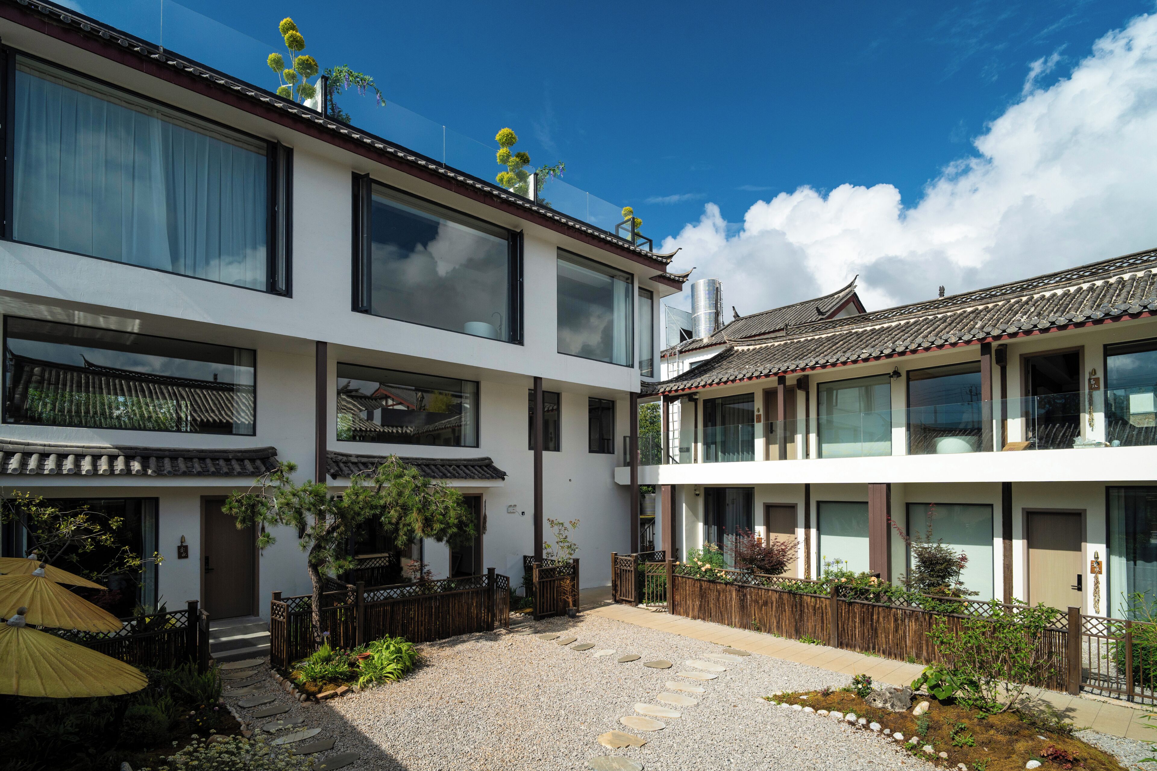 A traditional building with a modern extension, featuring a courtyard with a gravel path and potted plants.