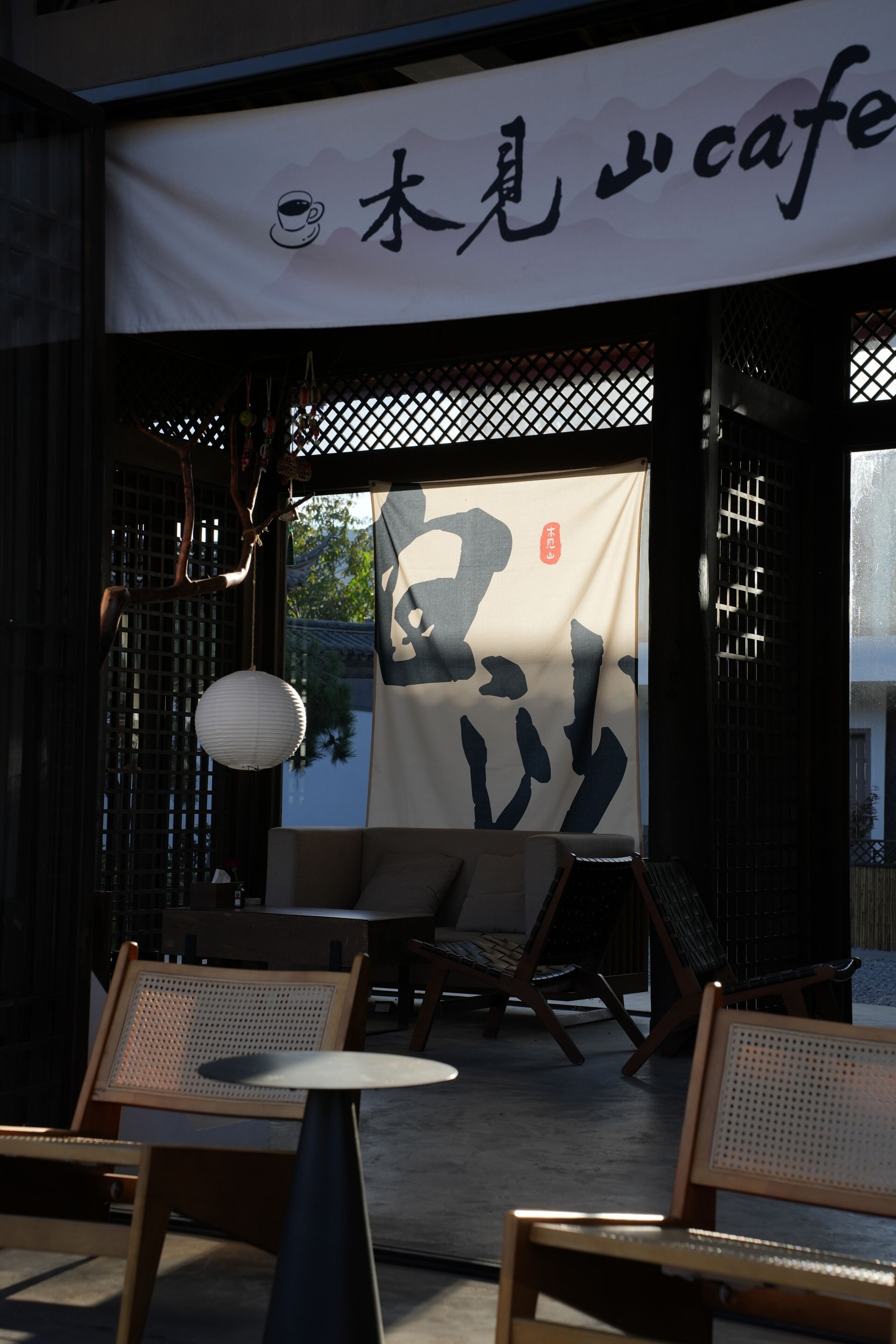 Un espacio al aire libre con mesas y sillas, un farol colgante y un gran cartel con caracteres japoneses.