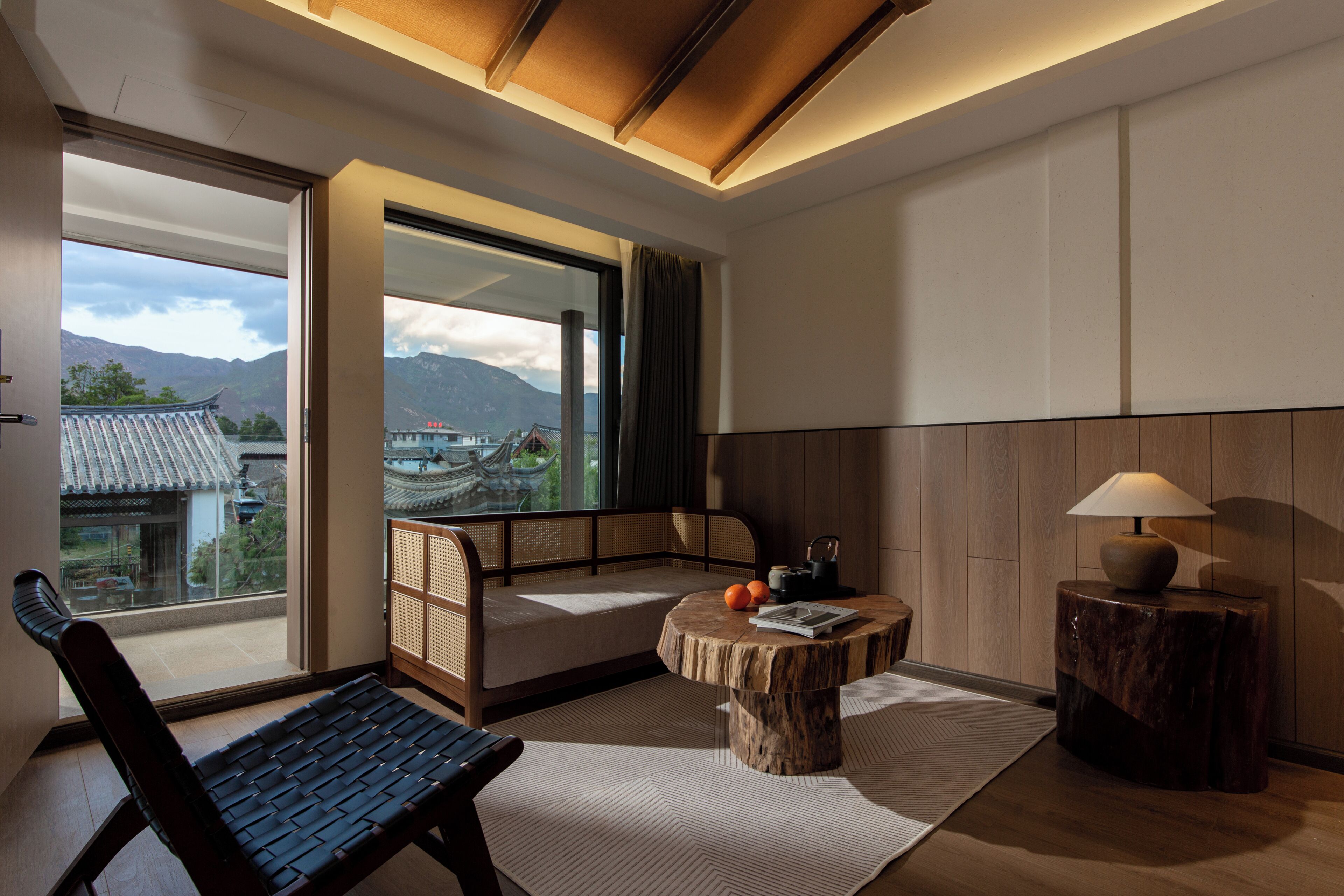 A room with a traditional Japanese-style sofa, a small round table with a book and oranges, and a view of mountains through large windows.