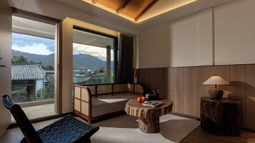 A room with a traditional Japanese-style sofa, a small round table with a book and oranges, and a view of mountains through large windows.