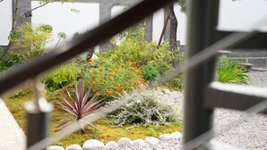 A garden with various plants and flowers, a stone pathway, and a metal railing in the foreground.