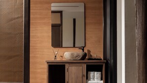 A bathroom with a wooden vanity, a mirror, a towel rack, and a stone on the counter.