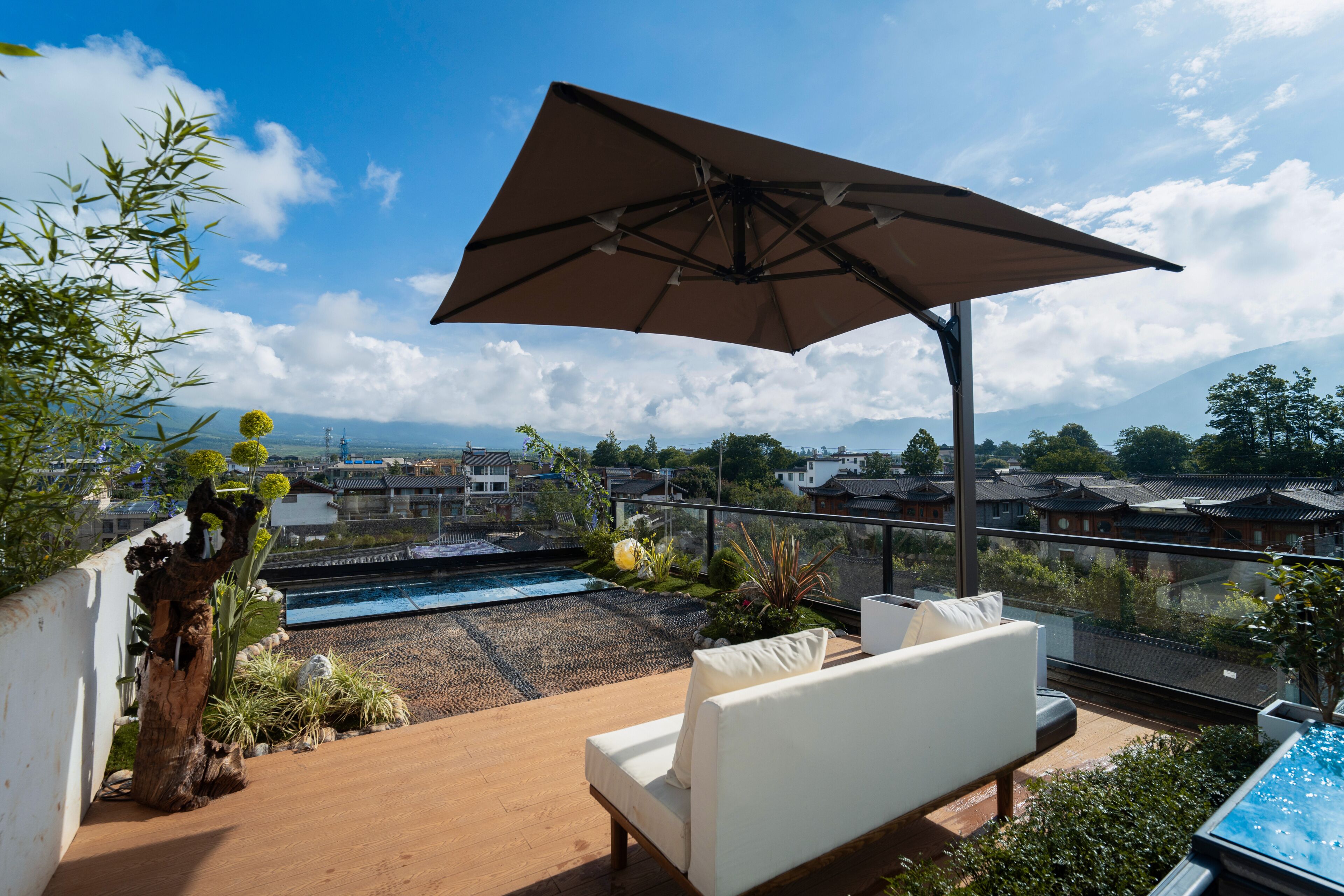 A rooftop terrace with a pool, white outdoor furniture, and a large umbrella.