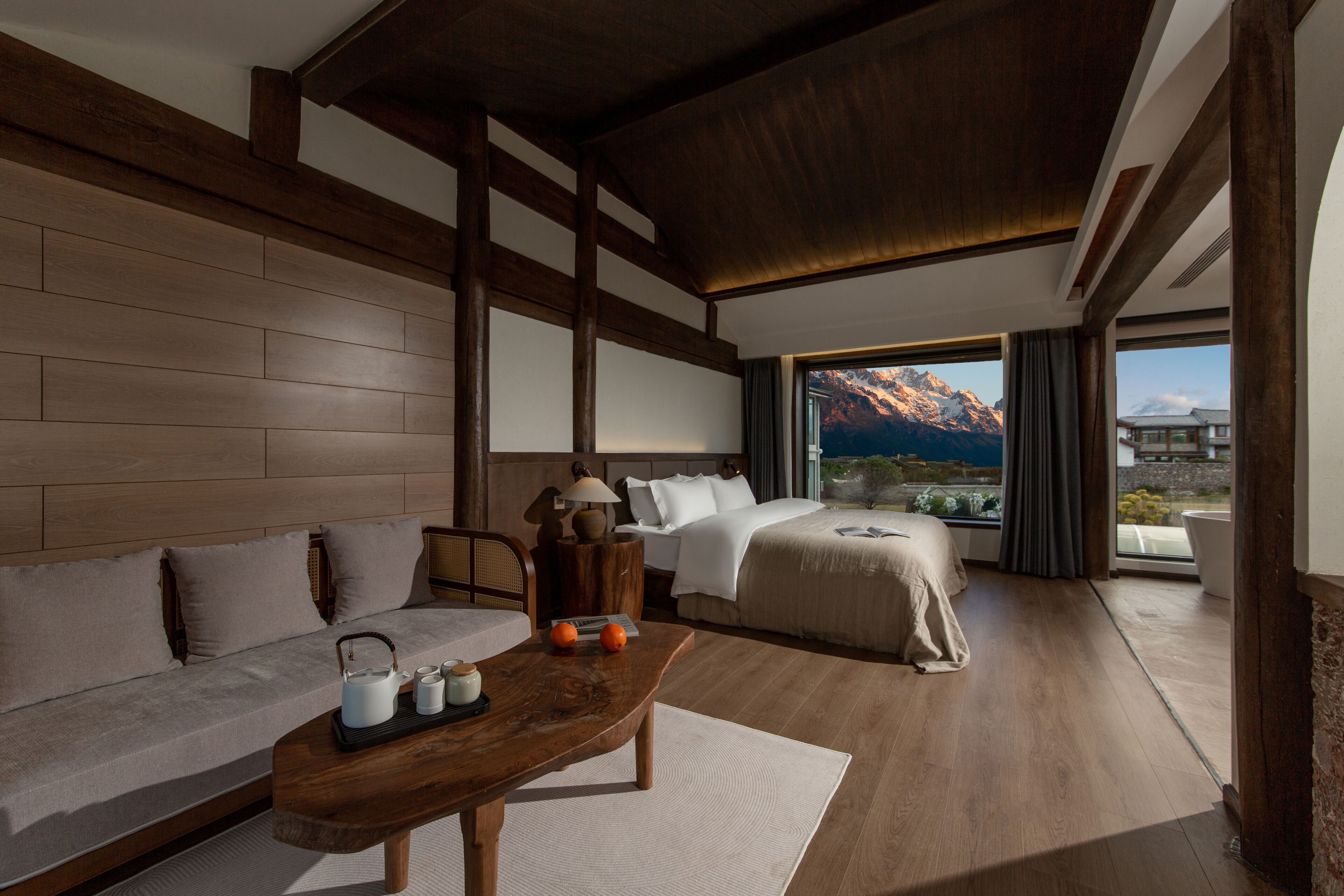 Une chambre d’hôtel avec un plancher en bois, un canapé, un lit, une table basse et une vue sur les montagnes par la fenêtre.