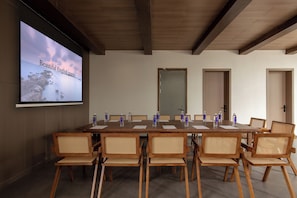A conference room with a long table, chairs, a projector screen, and doors.