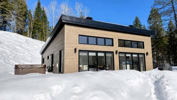 Un moderno edificio de dos pisos con grandes ventanales y techo plano, rodeado de nieve y árboles.