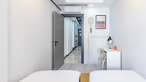 Ein modernes Hotelzimmer mit Bett, Schreibtisch und Stuhl, einer Tür zu einem Flur sowie einem Tennisschläger und Ball an der Wand.