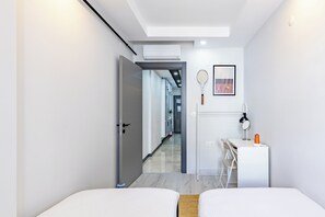 Ein modernes Hotelzimmer mit Bett, Schreibtisch und Stuhl, einer Tür zu einem Flur sowie einem Tennisschläger und Ball an der Wand.