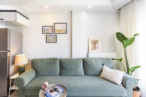 Ein modernes Wohnzimmer mit einem grauen Sofa, einem kleinen Couchtisch mit Zeitschriften, einer Lampe und gerahmten Kunstwerken an der Wand.