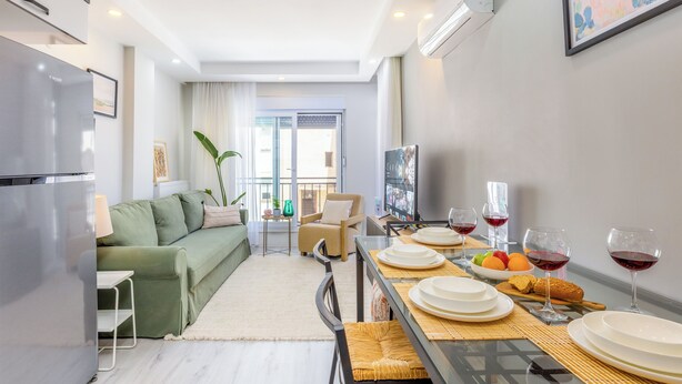 Ein modernes Wohnzimmer mit einer Couch, einem Esstisch gedeckt mit Tellern und Gläsern, und einem Fernseher.