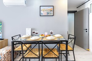 Un comedor con una mesa dispuesta para cuatro personas, sillas, una obra de arte enmarcada en la pared y una puerta a la derecha.
