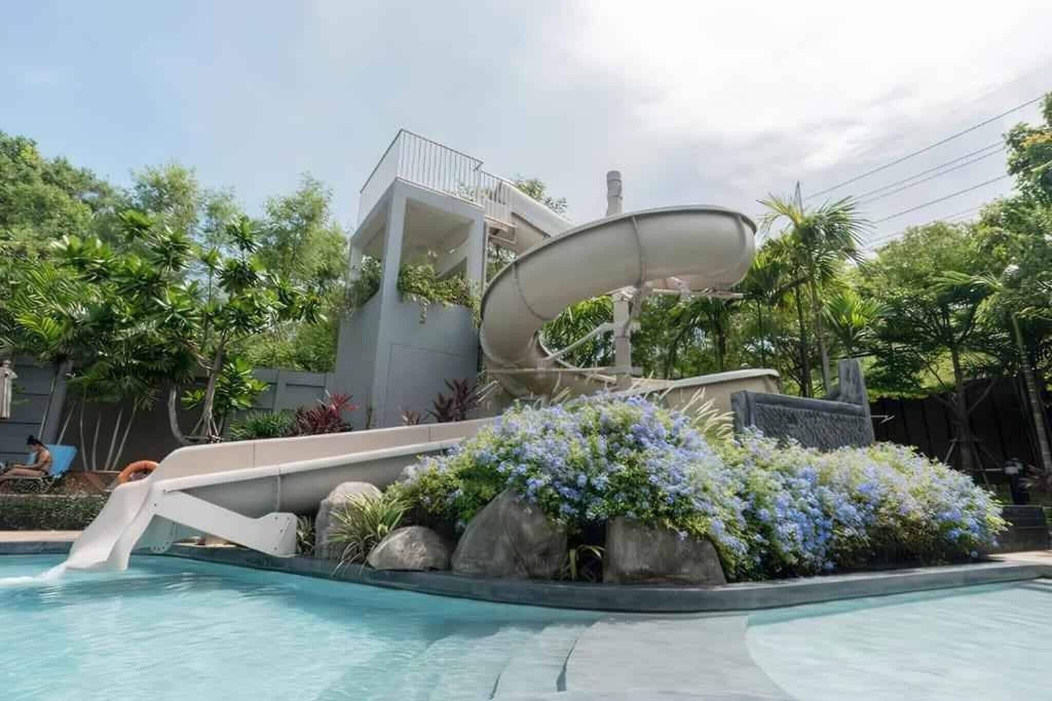 A swimming pool with a water slide and a small building with a balcony.