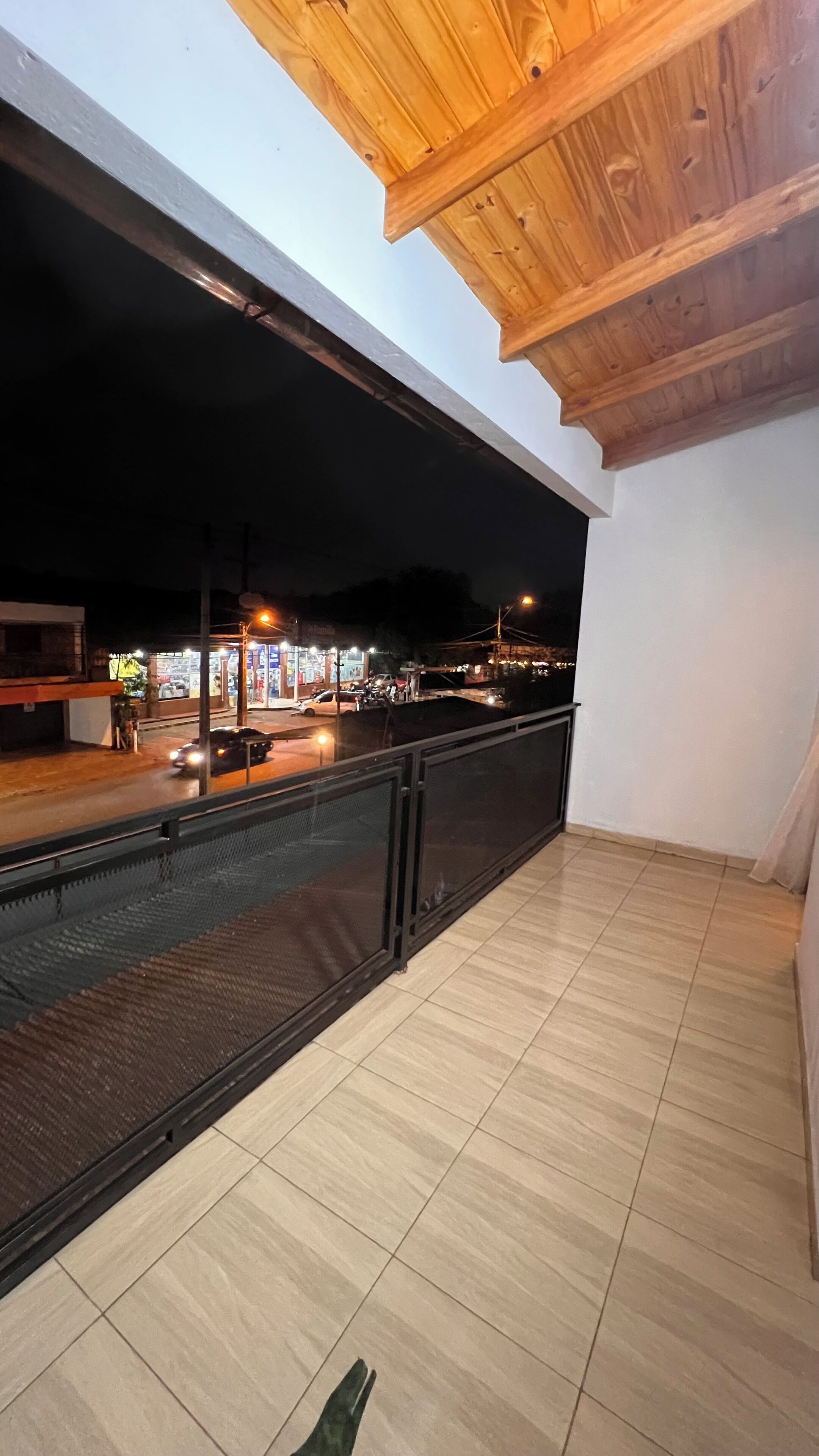 Un balcón con vista a una calle por la noche, que presenta suelo de baldosas y techo de madera.
