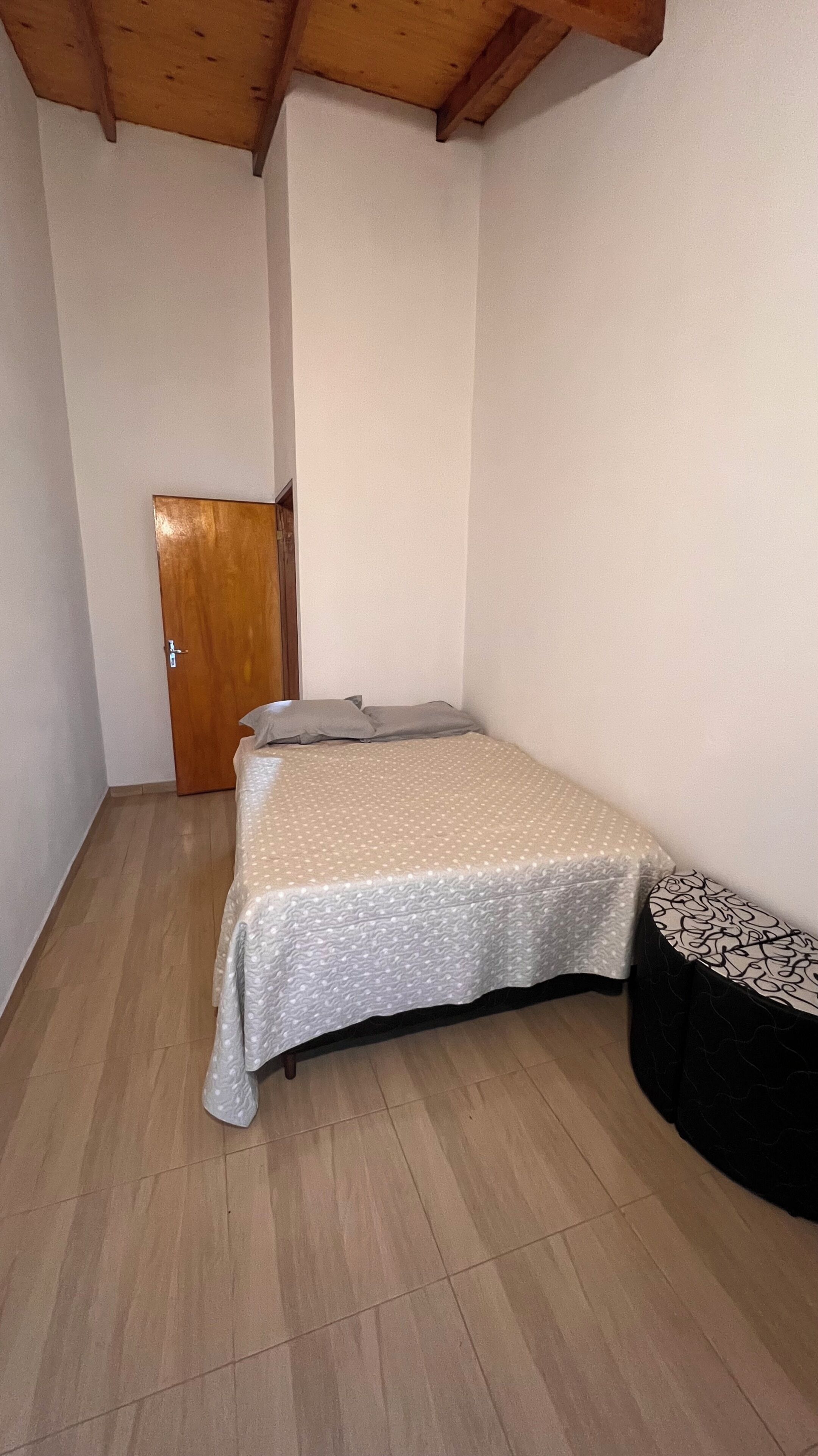 Una habitación pequeña con cama individual, puerta de madera, mesita de noche y colcha estampada.